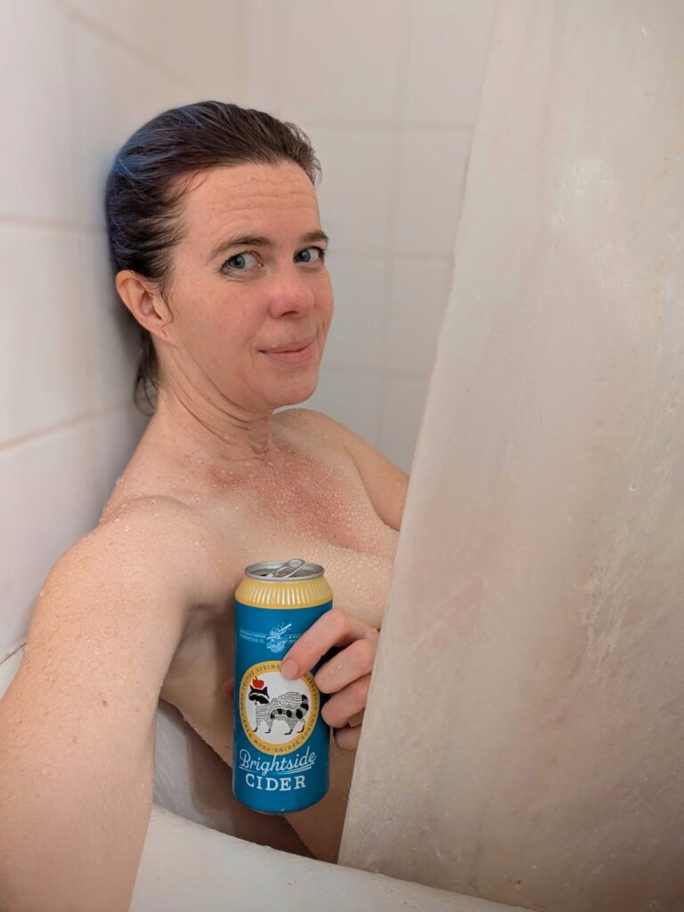 selfie of a person sitting in a bathtub holding a beer can up to cover their bare chest