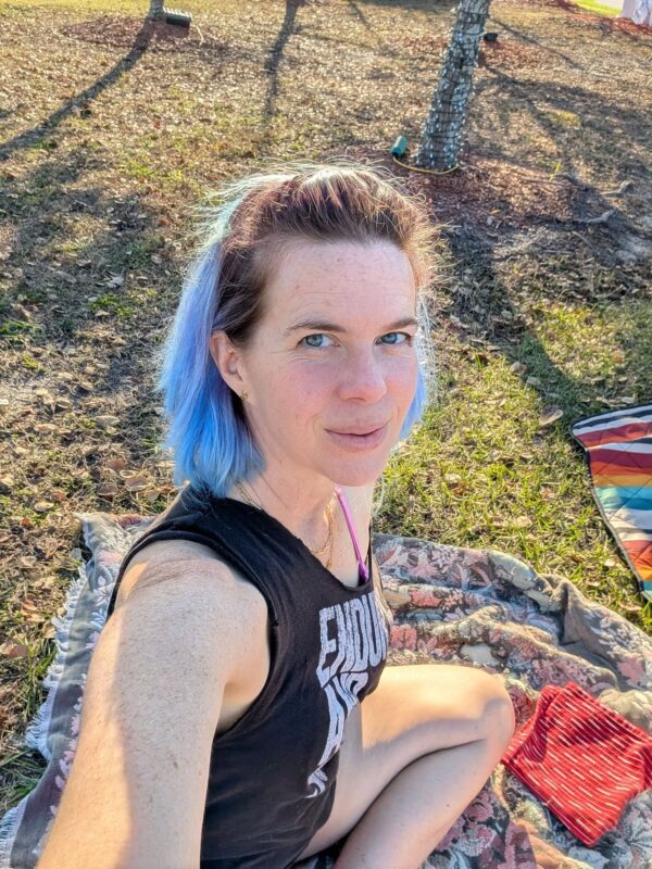 a person is sitting on a blanket on a patchy lawn in bright afternoon sunlight